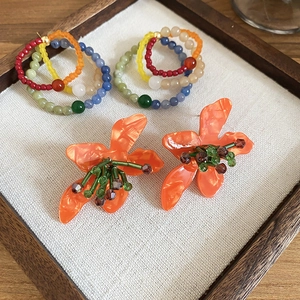 Close-up of bohemian beaded hoop earrings and orange floral studs with marble texture