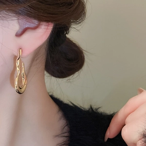 Close-up of a high-polish gold fluid wave earring on a model for a modern look