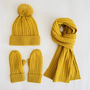 Flat lay of ginger yellow cable knit winter set with pompom hat, scarf and mittens