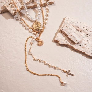 Detail showing faux pearls, golden conch charms and rhinestone cross on layered necklaces