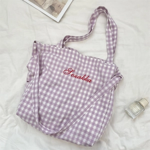 Detail of purple gingham tote bag featuring red embroidered text on soft cotton fabric