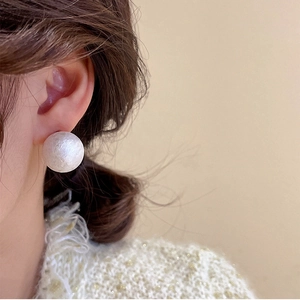 Close-up of minimalist white cotton pearl stud earring on model showing matte texture