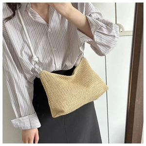 Detail of woven straw tote bag with white leather strap worn by a model in casual outfit