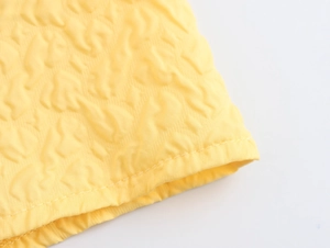 Detailed macro view of yellow dress fabric featuring 3D embossed texture and fine stitching