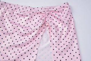 Detailed view of pink fabric with black polka dots featuring side ruching and split hem