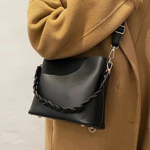 Black PU leather bucket bag with woven strap and metal feet on camel wool coat