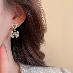 Gros plan d'une boucle d'oreille cœur noir et nœud papillon sur une oreille féminine