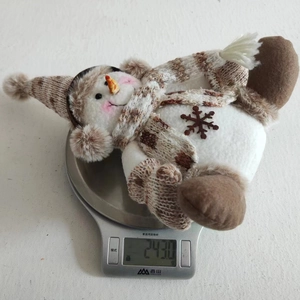 Detail shot showing a plush snowman Christmas ornament weighing 243g on a digital kitchen scale