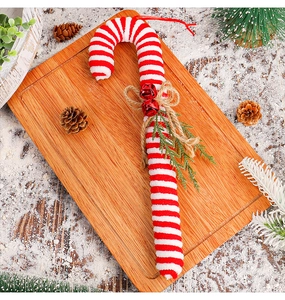 Detail of red and white knitted candy cane ornament with a bell and pinecone on wood