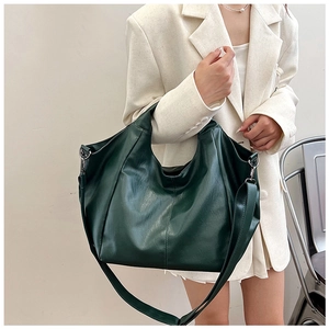 Detail of dark green textured leather tote bag worn as a shoulder bag on a light suit