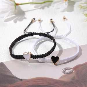 Detail of adjustable hand-woven couple bracelets with heart pendants in black and white