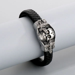 Close-up of woven black leather bracelet with silver skull charm and retro metallic finish