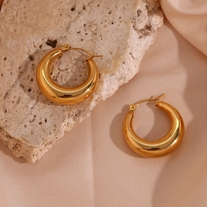 Close-up of golden chunky hoop earrings on textured stone and silk fabric background