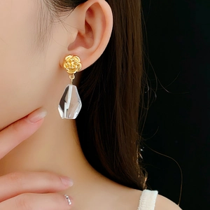 Detail of golden flower earring with clear geometric glass pendant worn on model
