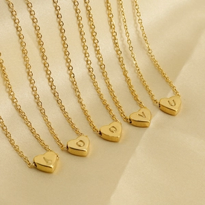 Gros plan de pendentifs cœur en or 18 carats avec lettres sur chaînes en acier inoxydable