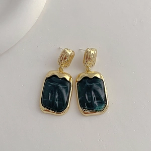 Detailed close-up of vintage resin earrings with gold edges and green marble texture