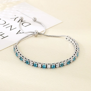 Detail of adjustable silver steel bracelet with blue and clear zircon stones on textured backdrop