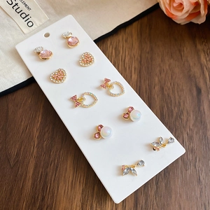 Close-up of six pairs of gold earrings with pink rhinestones and pearls on display card