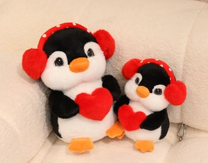 Close-up of plush penguin doll pair with red ear muffs and heart detail on soft fabric