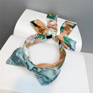 Close-up of fabric headband featuring a satin bow and floral pattern on white stand