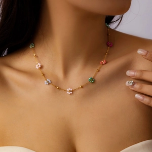 Close-up of golden necklace with colorful resin flower charms and beads on model's collarbone