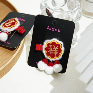 Detail of red plush hair clip with Lucky embroidery and hanging white pom poms