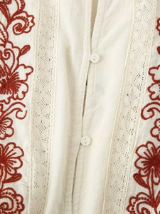 Detailed close-up of white cotton blouse with red floral embroidery and lace trim details