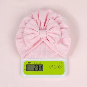 Pink newborn turban hat with large bow on scale showing lightweight 23.4g texture