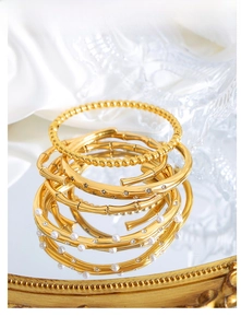 Detailed close-up of stacked gold bangles with pearls and crystals on silk background
