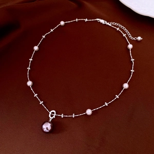 Detail of adjustable pearl necklace featuring a large dark pendant on silk fabric