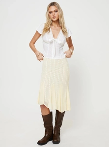 Détail d'un haut à lacets blanc avec une jupe beige tissée et des bottes en cuir marron foncé