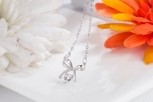Detail of silver bow necklace with heart-shaped crystal on white decorative plate