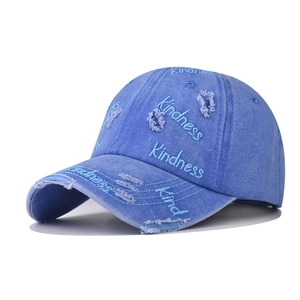 Close-up of distressed washed blue denim baseball cap featuring Kindness embroidery