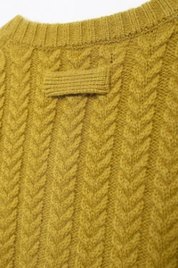 Detail showing ginger yellow cable knit texture and decorative back collar strap