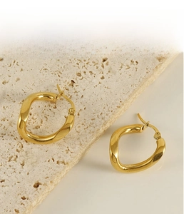 Detailed view of irregular twisted gold hoop earrings on a textured stone display
