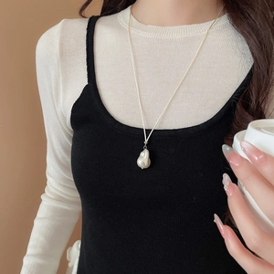 Close-up of a white baroque pearl pendant necklace worn by a model on a slender chain