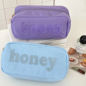 Detail of nylon toiletry bag with large honey towel embroidery and secure gold zipper