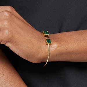Elegant gold open cuff bracelet featuring two square green gemstones on a black background