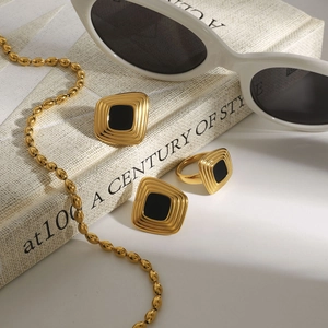 Vintage gold-plated jewelry set with square black enamel studs and ring on a book