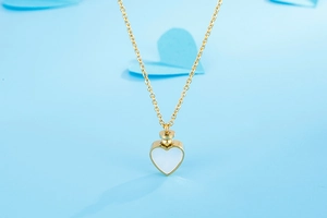 Gros plan d'un collier urne cœur doré avec nacre blanche sur fond bleu clair