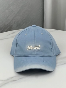 Detailed view of light blue cotton baseball cap featuring heart embroidery and distressed rips