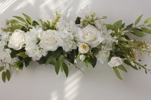 Detailed view of long white artificial rose floral arrangement with green leaves