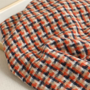 Close-up of thick British plaid fabric in orange, black, and beige cashmere-like texture