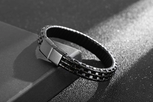Detailed view of black braided leather bracelet with matte metal magnetic clasp on grey base