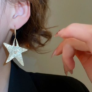 Close-up of hammered gold star earring showing the irregular metallic texture on a model