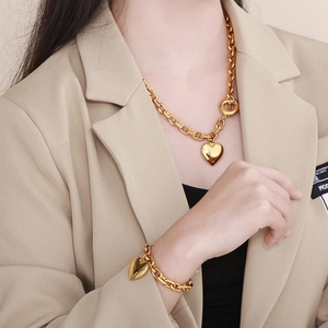 Close-up of golden thick chain jewelry set with heart pendants on a model in a beige blazer