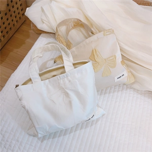 Detail of canvas mini bags with bow appliqué and zip closure in white and beige tones