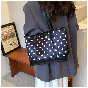 Fashionable black tote bag with white polka dots shown on shoulder in a minimalist setting