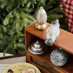 Space-themed Christmas ornaments featuring astronauts and rockets on a wood cabinet
