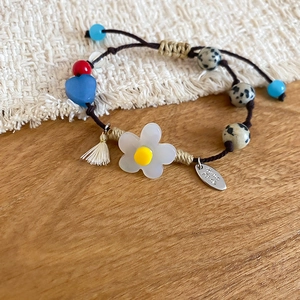 Détail d'un bracelet perlé fait main avec fleurs en résine, pierres et cordon réglable